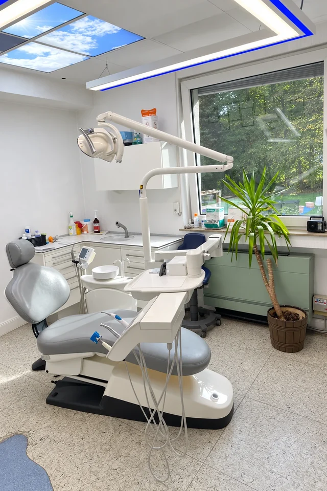 Behandlungszimmer mit grauem Behandlungsstuhl und großem Fenster